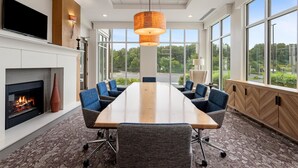 Un salón de conferencias con una larga mesa, sillas azules, chimenea y ventanas amplias que dan a vistas de follaje.