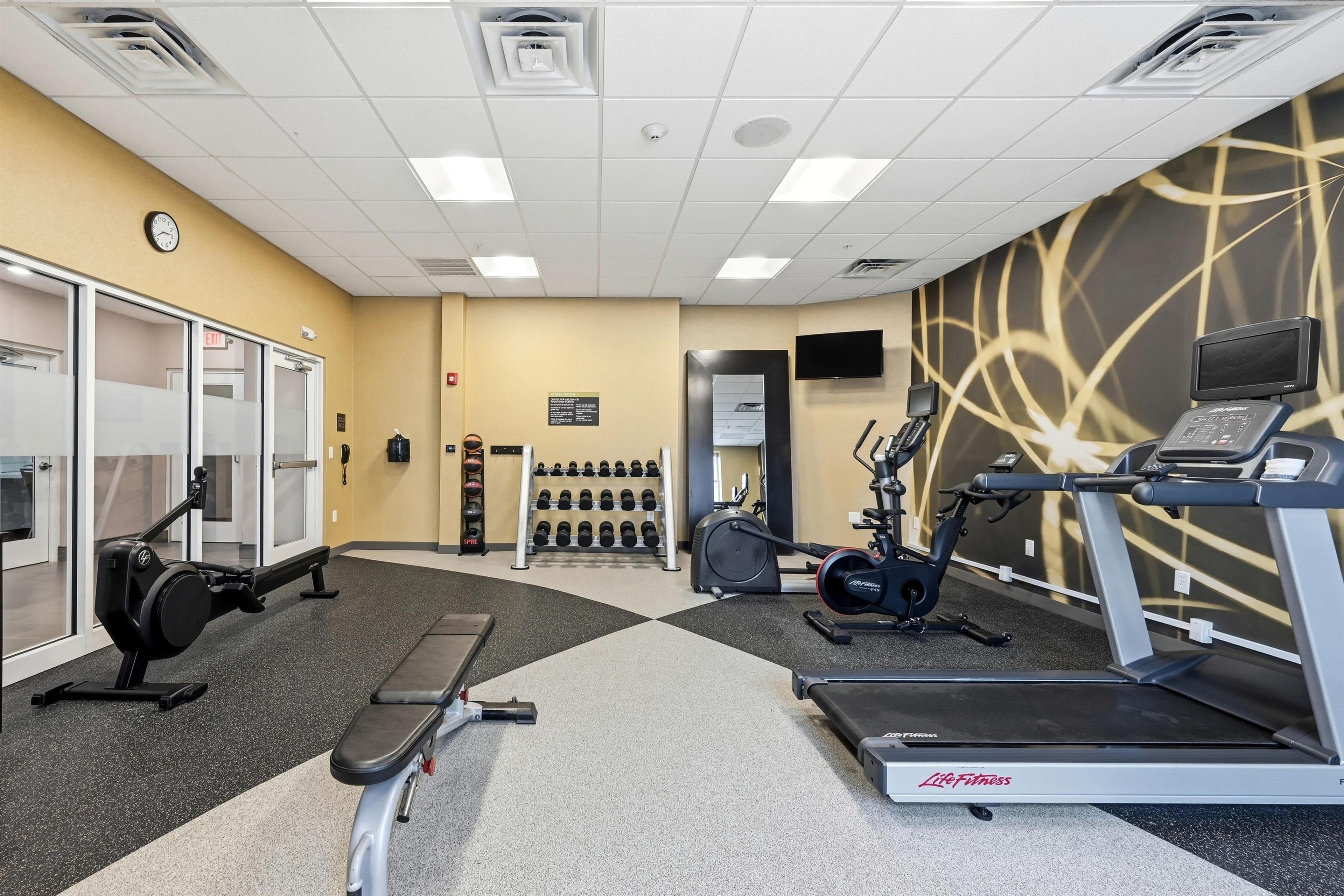 A fitness center with cardio equipment, weight machines, and a wall-mounted TV.