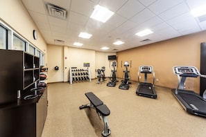 Un gimnasio con cintas de correr, elípticas, una banca y un estante con mancuernas.