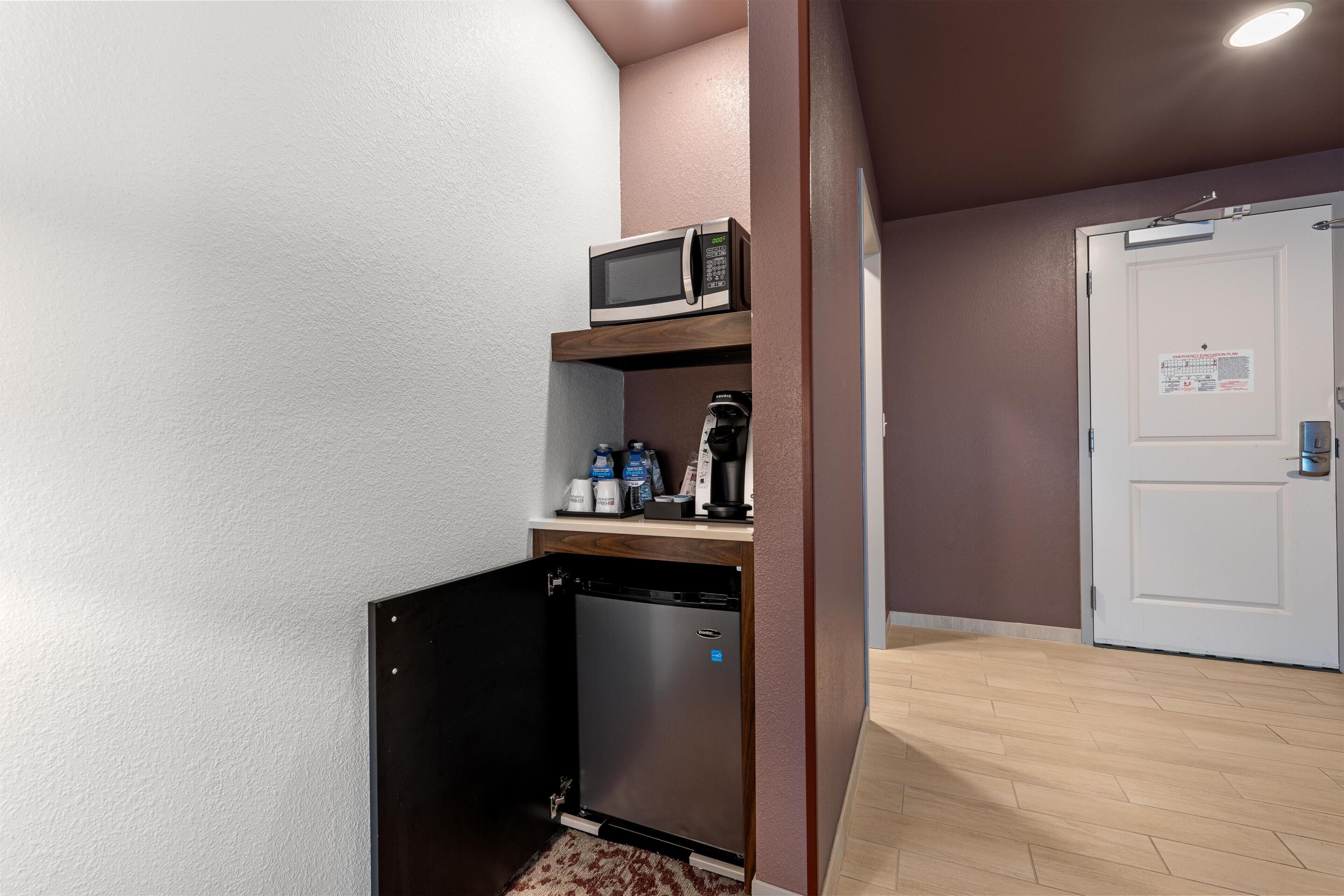 Una kitchenette compacta con microondas, cafetera y refrigerador.