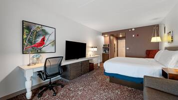 A hotel room with a bed, desk, TV, and artwork.