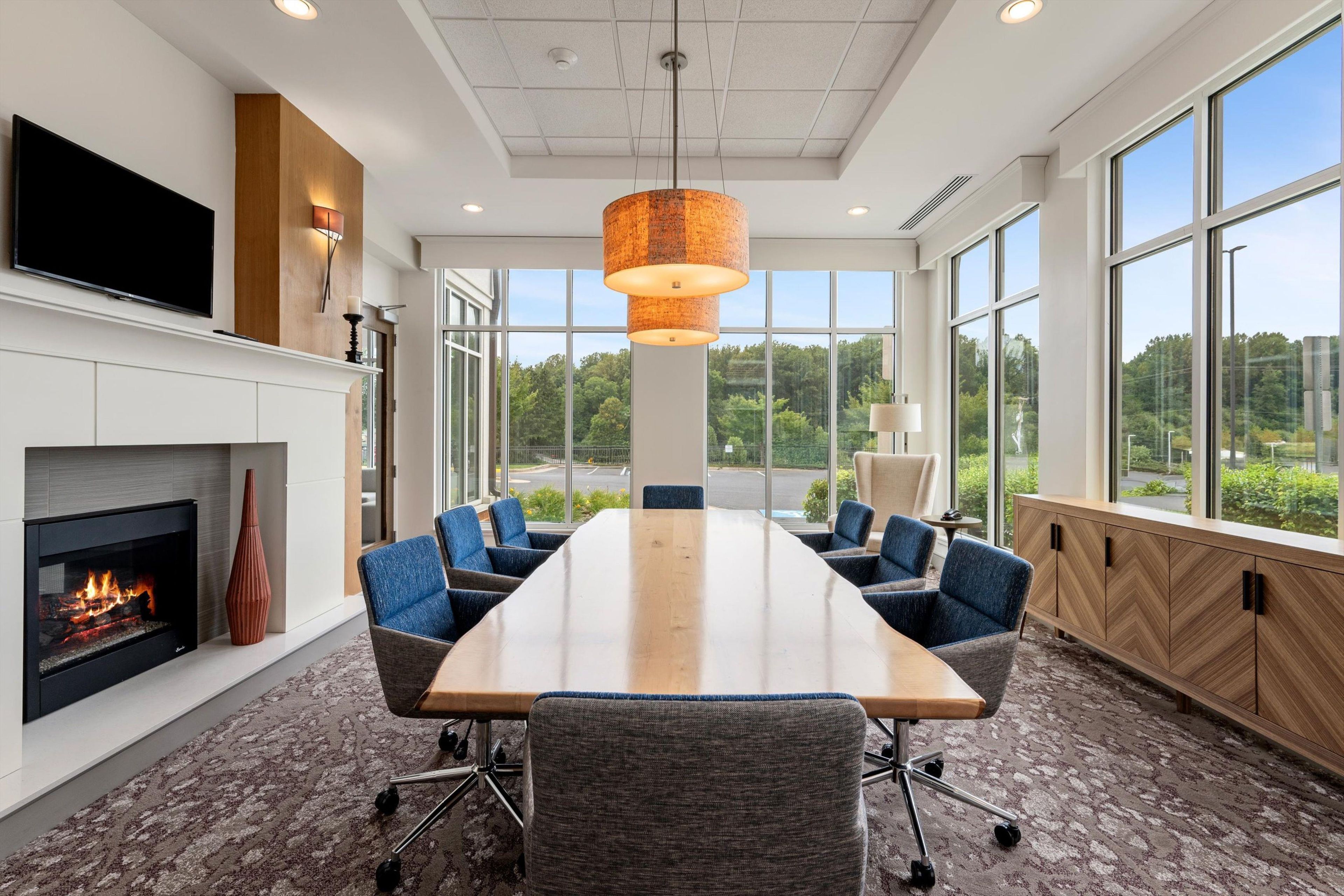 A conference room with a long table, chairs, a fireplace, and large windows offering a view of the outdoors.