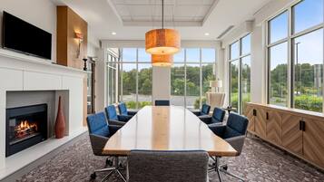 A conference room with a long table, chairs, a fireplace, and large windows offering a view of the outdoors.