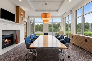 A conference room with a long table, chairs, a fireplace, and large windows offering a view of the outdoors.