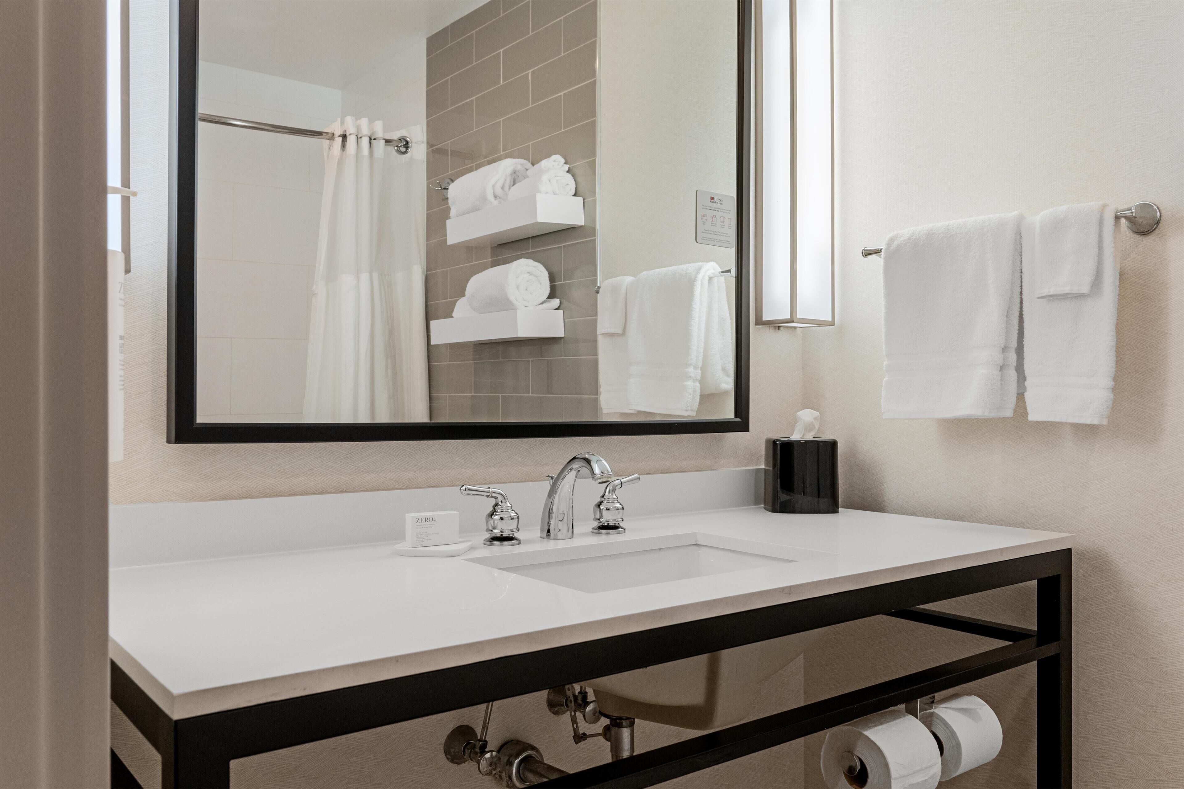 A bathroom with a white sink, a large mirror, and a towel rack with white towels.