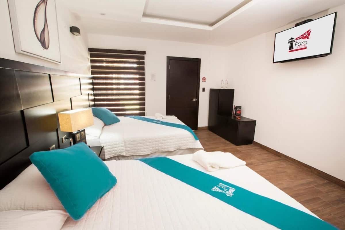 Habitación de hotel con dos camas, televisor, escritorio y ventana con persianas.