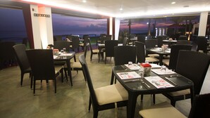 Un restaurante con mesas y sillas, vista al atardecer y un letrero con el nombre del restaurante.
