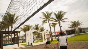 Una cancha de voleibol de playa con una red, palmeras y un edificio al fondo.