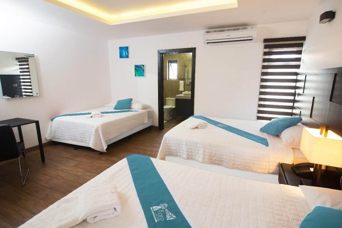 Habitación de hotel con dos camas, un escritorio y un baño visible a través de una puerta abierta.
