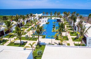A resort with a central pool surrounded by palm trees and a view of the ocean. - Hotel El Faro (Taxisco)