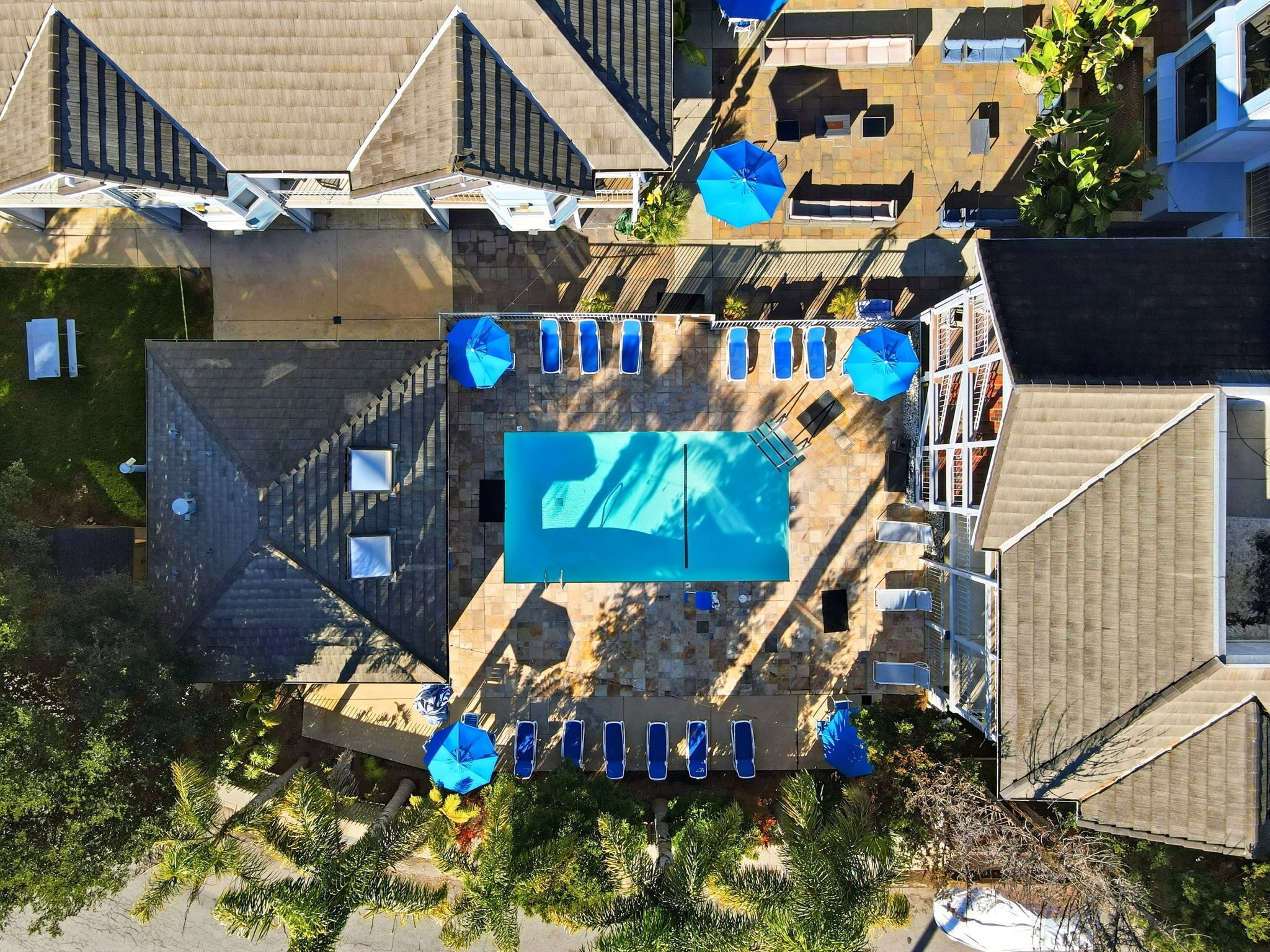 An aerial view of a residential area with a swimming pool surrounded by lounge chairs and umbrellas, indicating a private outdoor space.