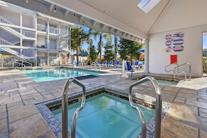 Uma área de piscina com várias piscinas, espreguiçadeiras e um espaço de estar coberto.