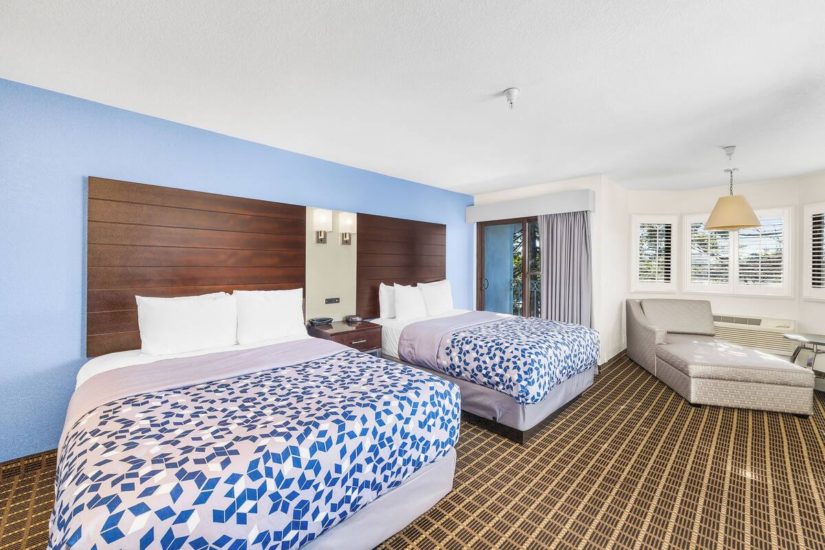 A hotel room with two beds, a sofa, a small table, and a window with blinds.