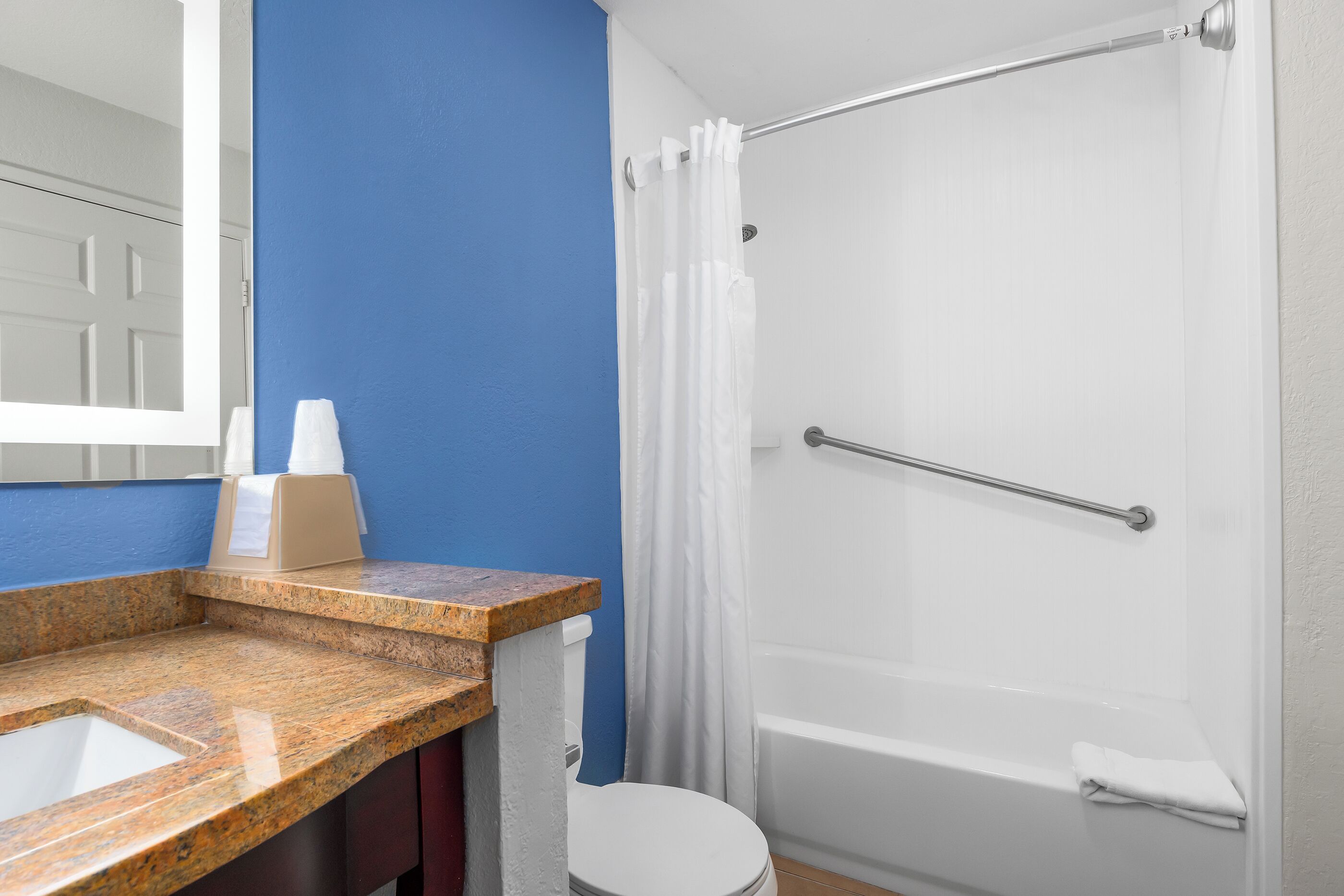 Une salle de bain dotée d’un comptoir en granit, de toilettes blanches et d’une douche à l’italienne avec une porte en verre.