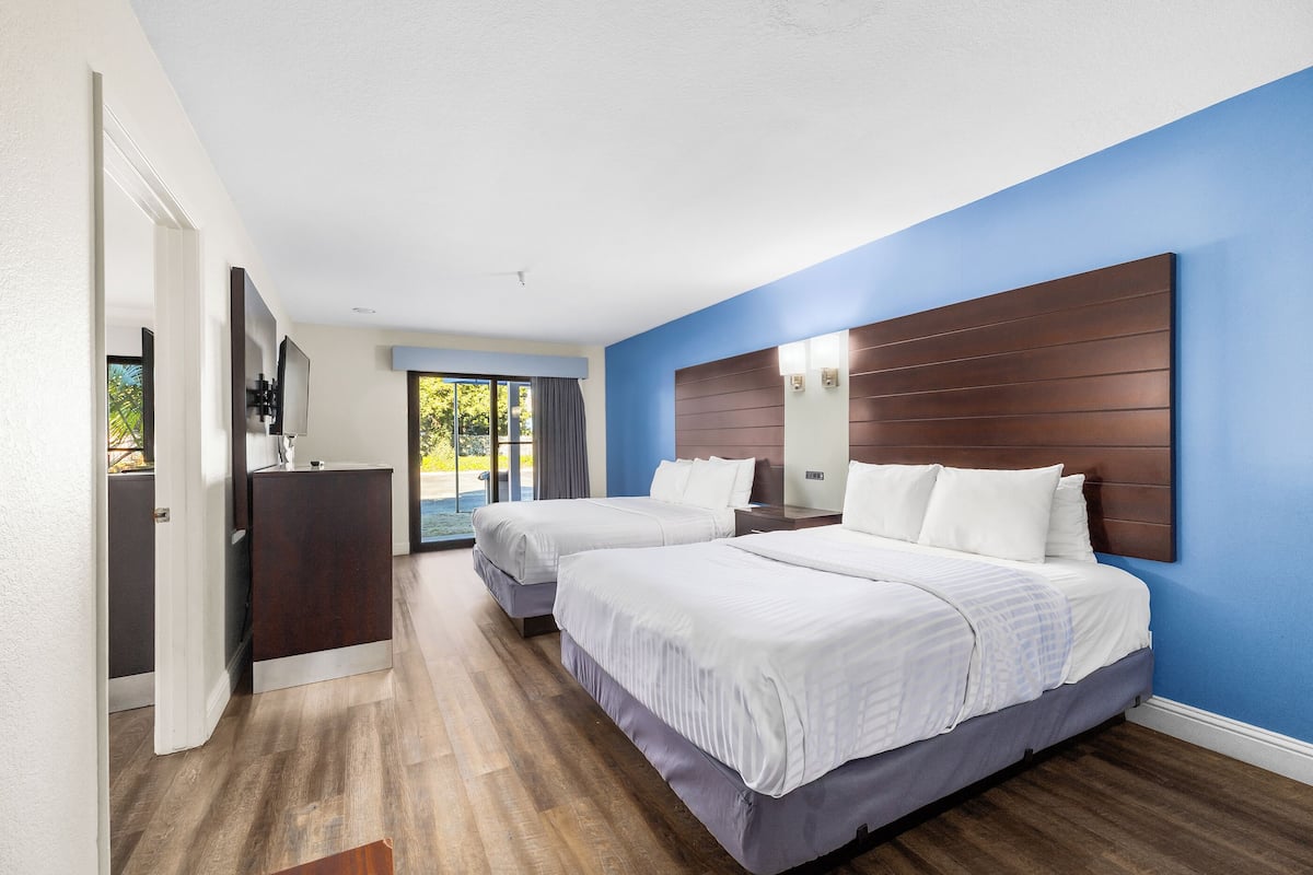 A hotel room with two beds, a wooden headboard, a desk, and a large window.