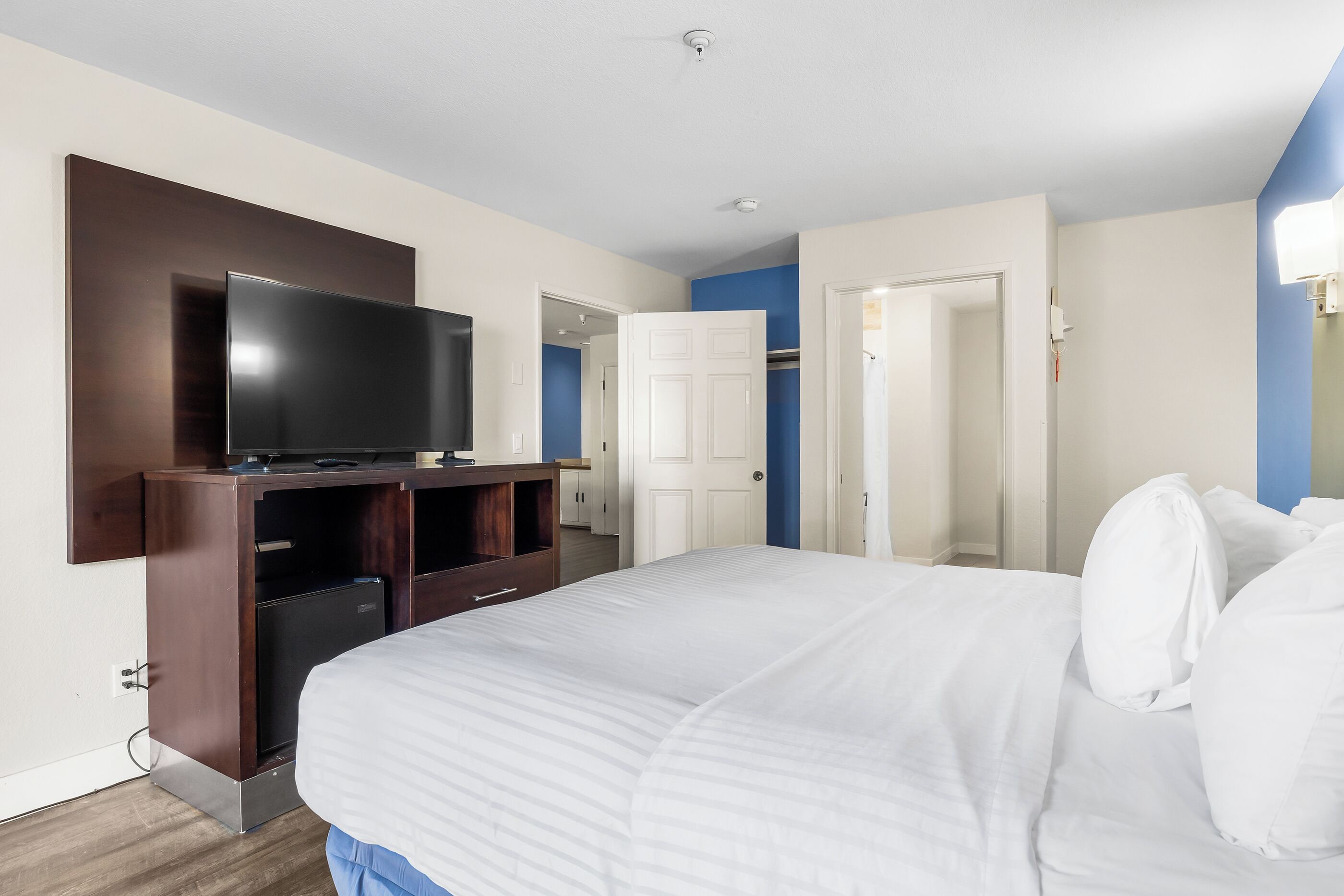 A hotel room with a large bed, a flat-screen TV, a wardrobe, and a door leading to a bathroom.