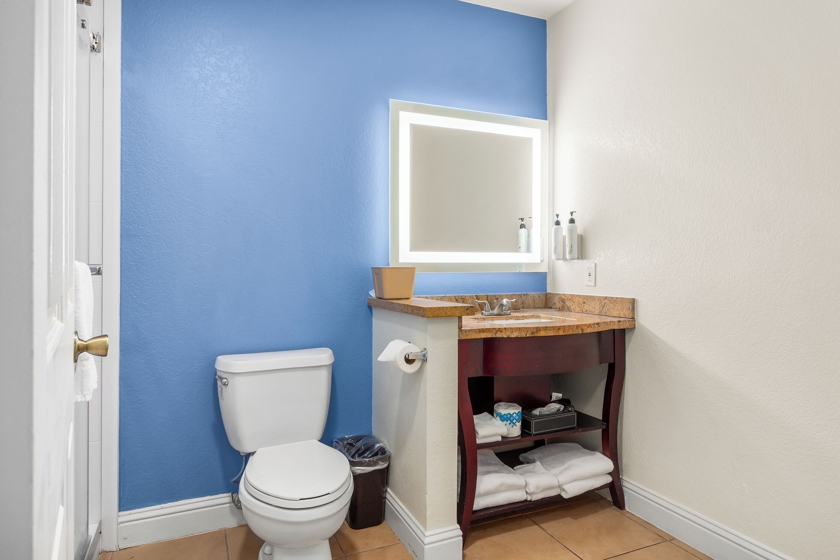 A bathroom with a blue wall, white toilet, and a vanity with a mirror and shelves.