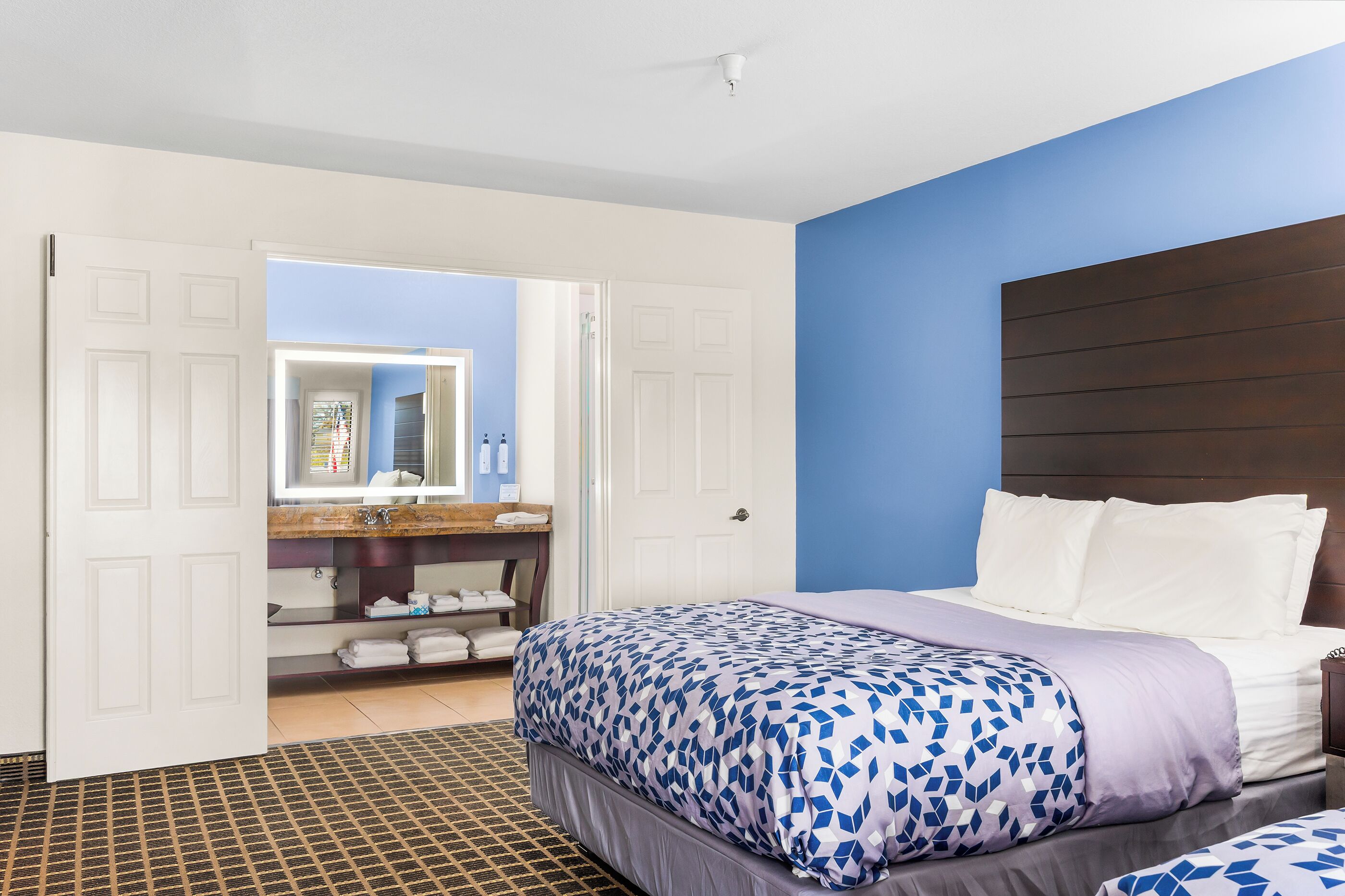 A bedroom with a bed, a bathroom with a mirror, and a door leading to another room.