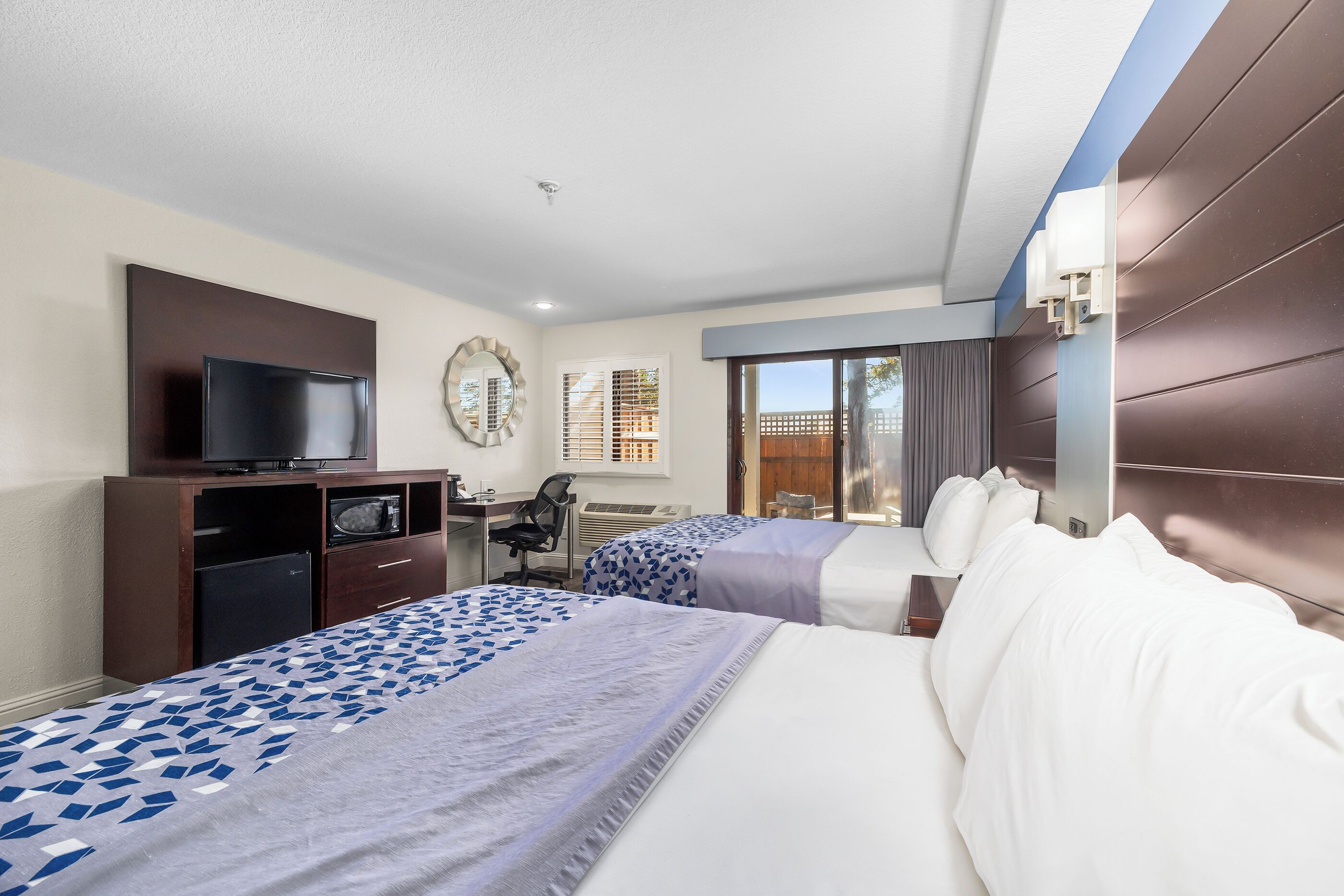 A hotel room with two beds, a desk with a computer, a television, and a window with blinds.