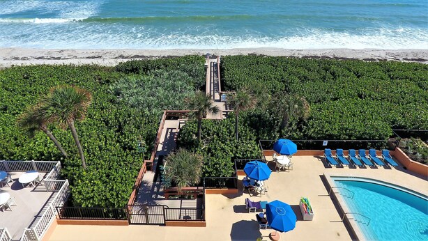 Un espace piscine aménagé sur le toit, avec des chaises longues et des parasols, offrant une vue sur une plage et l’océan.