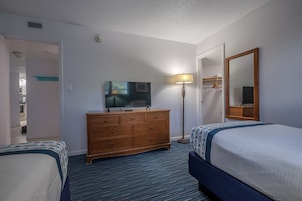 Quarto de hotel com duas camas, televisão, penteadeira, abajur e espelho.