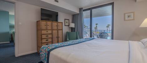 A hotel room with a large bed, a wooden wardrobe, a chair, a balcony with a view, and a door leading to another room.