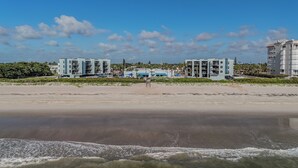 A beachfront hotel with multiple buildings, a sandy beach, and waves in the foreground.