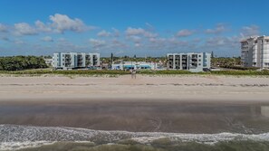 A beachfront hotel with multiple buildings, a sandy beach, and waves in the foreground.