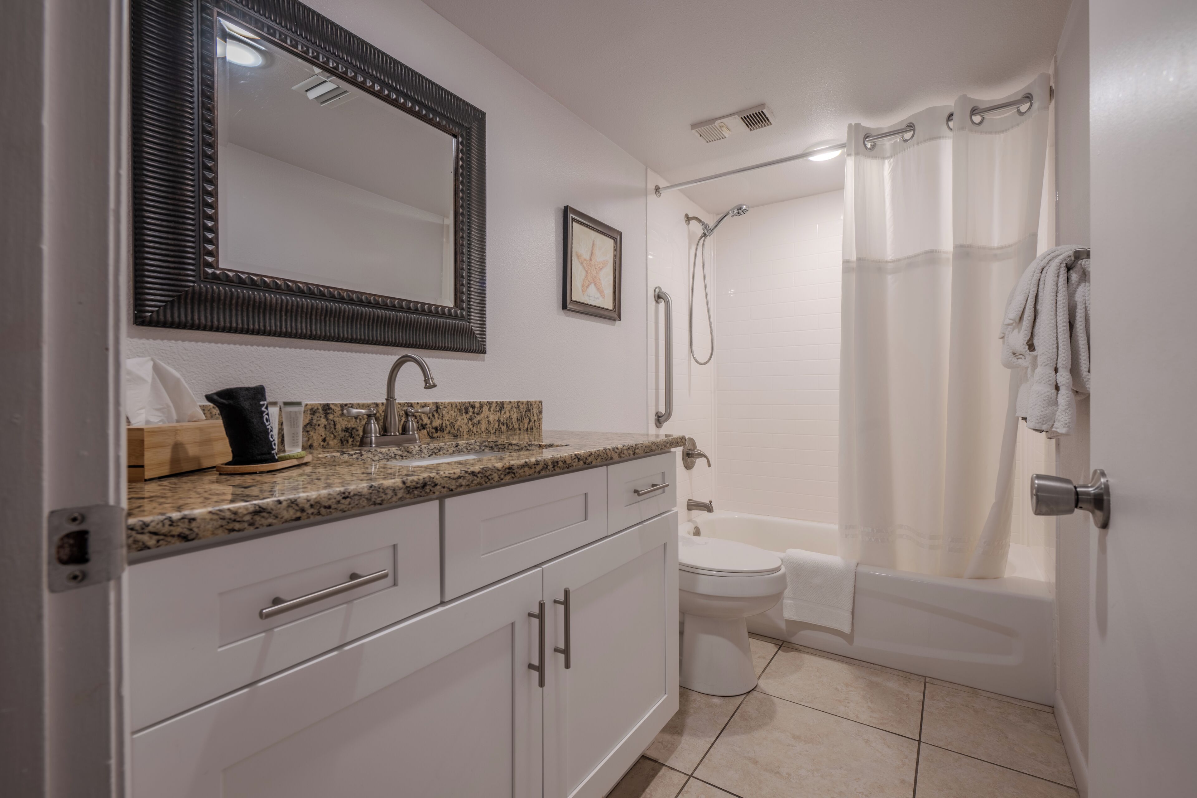 A bathroom with a granite countertop, a white toilet, a shower with a glass door, and a large mirror above the sink.