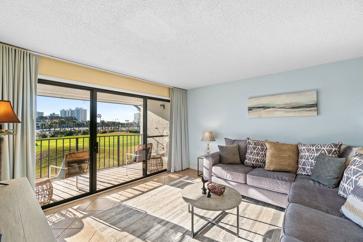 Un salon moderne avec un canapé, une table basse et une vue sur un terrain de golf et le paysage urbain, grâce à de grandes portes coulissantes.