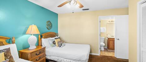 A bedroom with two beds, a ceiling fan, a nightstand with a lamp, and a bathroom visible through an open door.