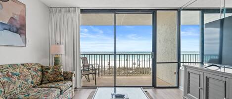 A living room with a sofa, a glass coffee table, a cabinet, and a view of the beach through a sliding glass door.
