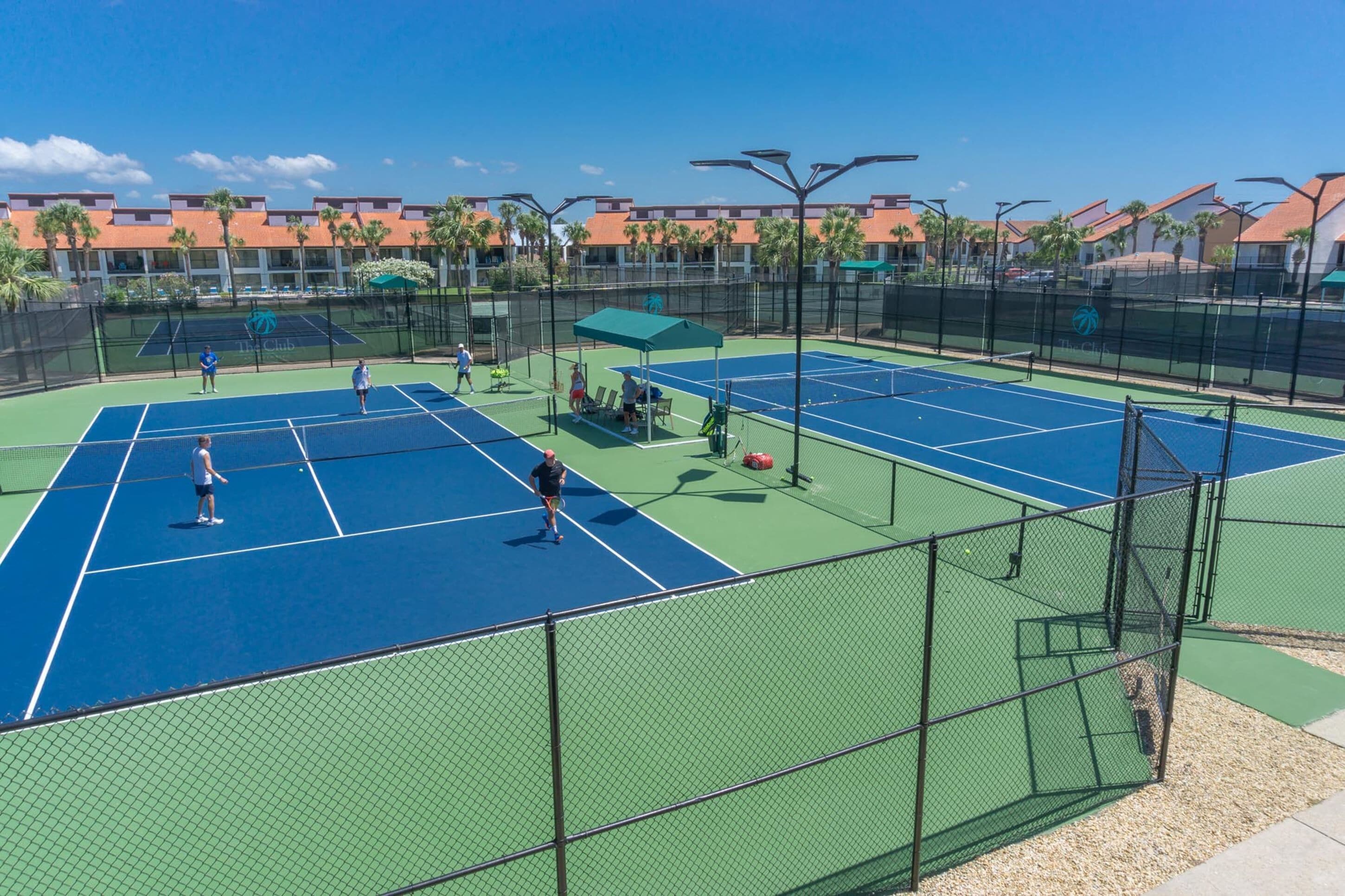 Un court de tennis comprenant plusieurs terrains, une zone de sièges abritée et une clôture entourant le terrain.