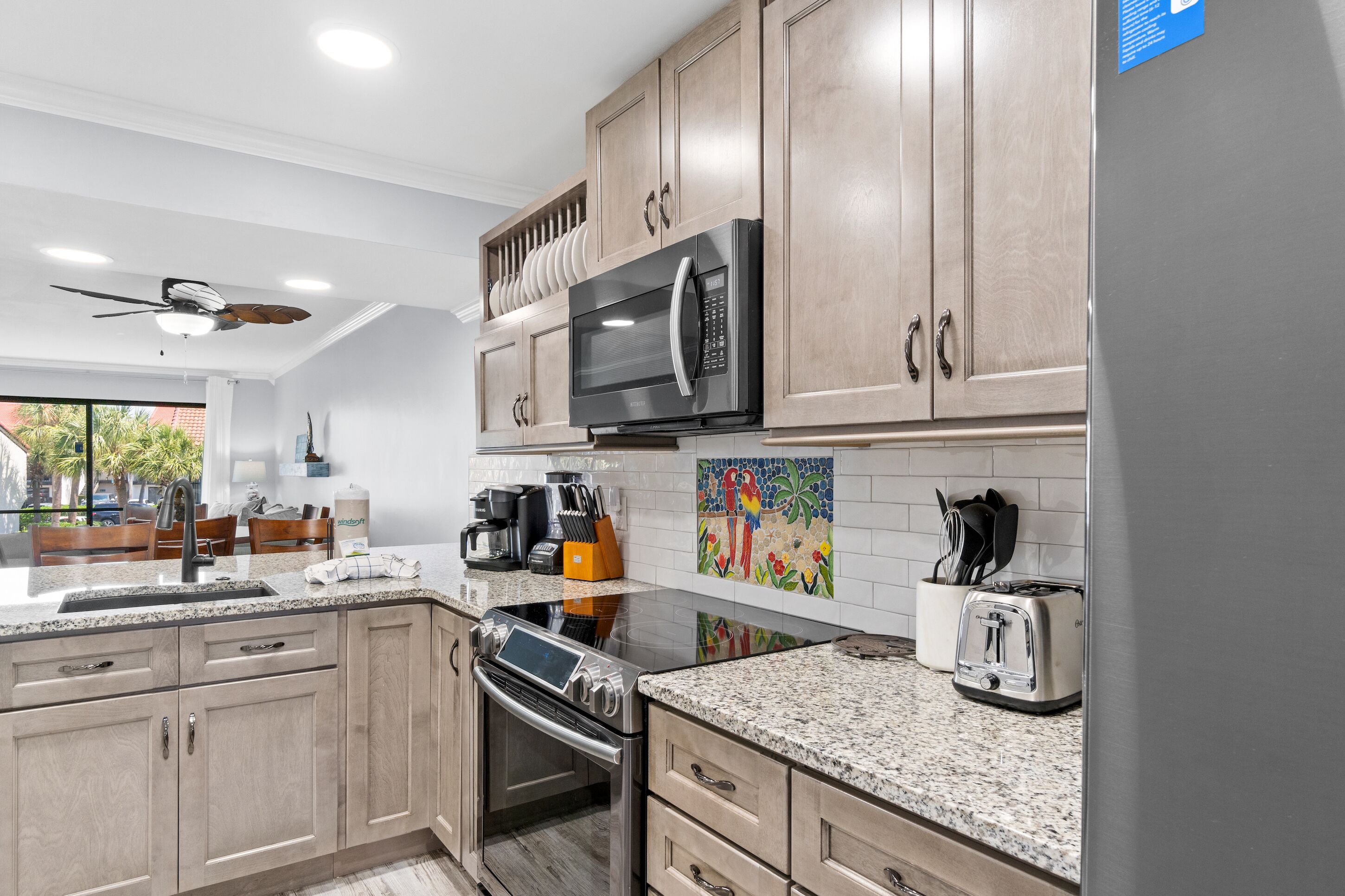 A modern kitchen with light wood cabinets, a stainless steel microwave, a built-in oven, and a toaster.