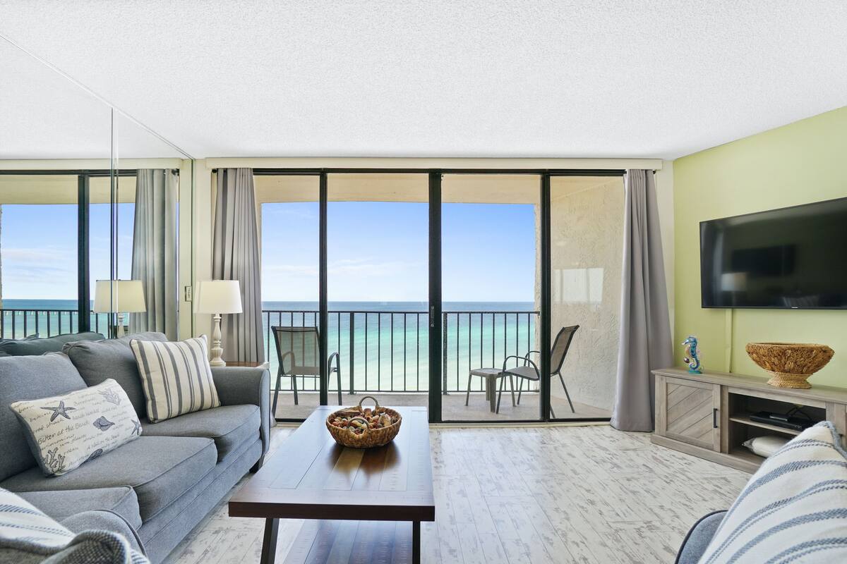 Un salon moderne avec un canapé, une table basse et un téléviseur. Il y a un balcon avec vue sur l’océan.