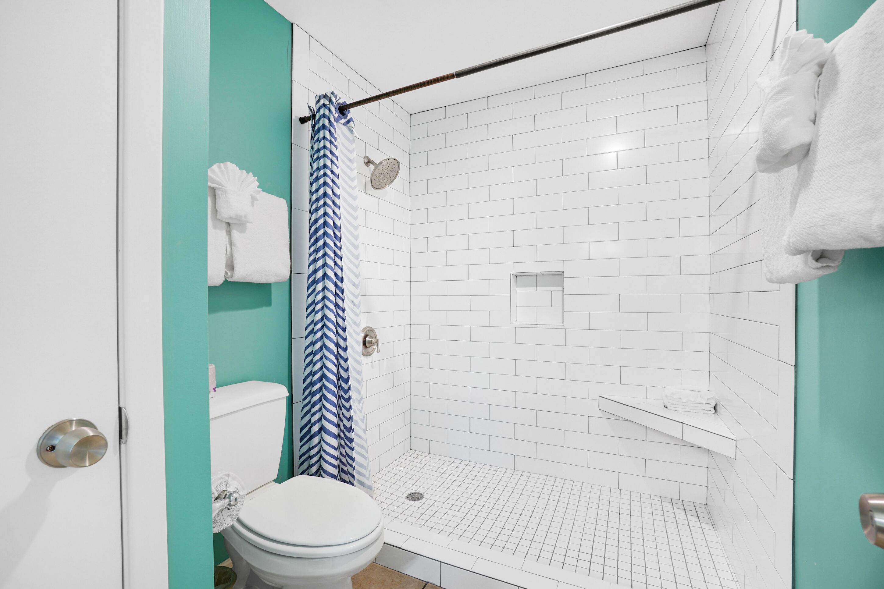 Une salle de bain moderne avec des toilettes blanches, une douche dotée d’un rideau de douche à rayures bleues et blanches, et un lavabo blanc avec un porte-serviettes.