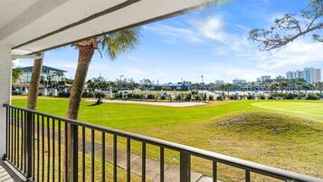 A view from a balcony overlooking a well-maintained lawn with a golf cart, palm trees, and a cityscape in the background.