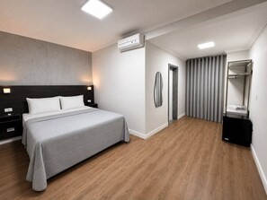A modern hotel room with a large bed, bedside tables, an air conditioning unit, a wardrobe, and a mirror. - Hotel Diamante (São Paulo)
