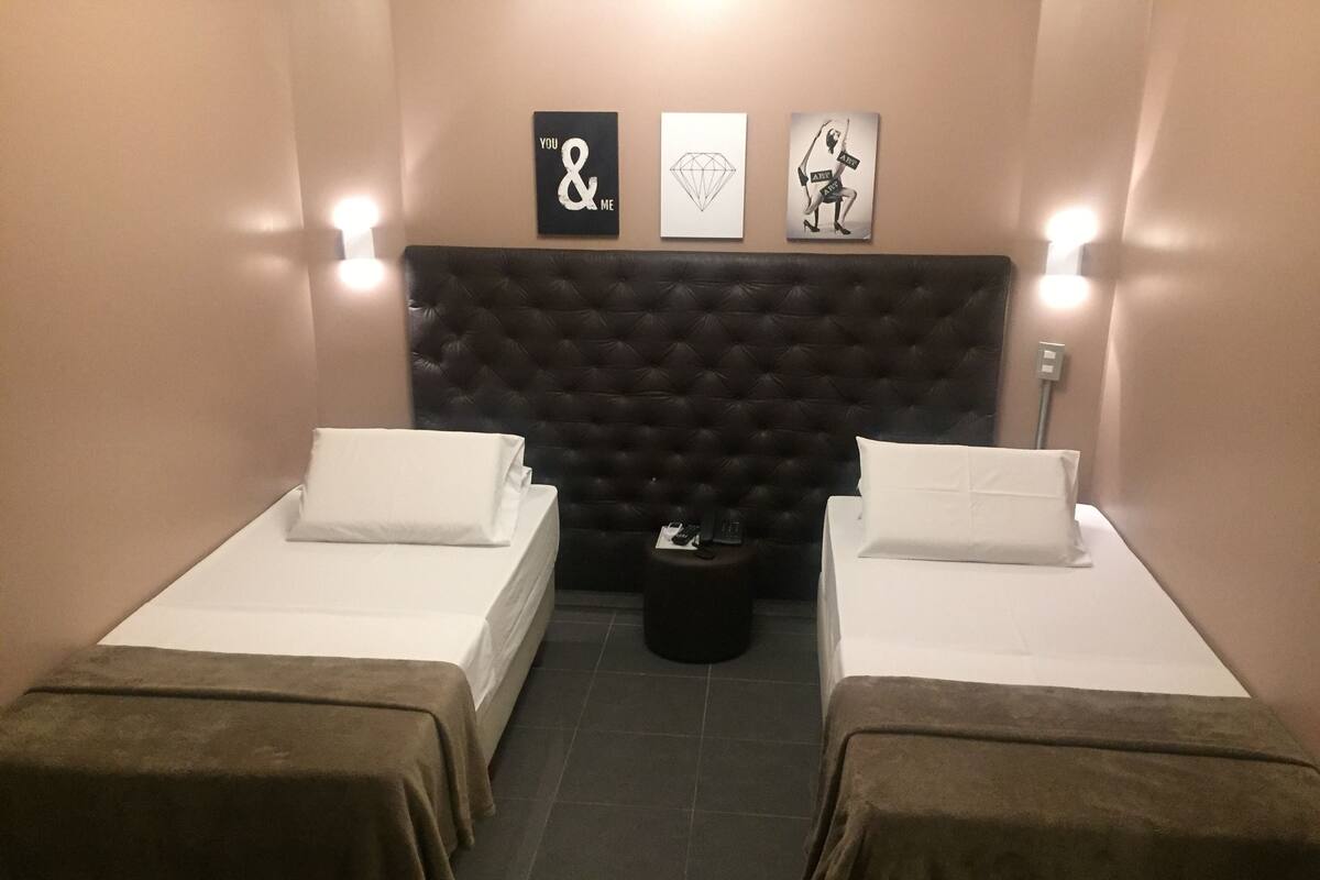 Een hotelkamer met twee bedden, een donker geweven hoofdeinde en drie kunstwerken aan de muur.