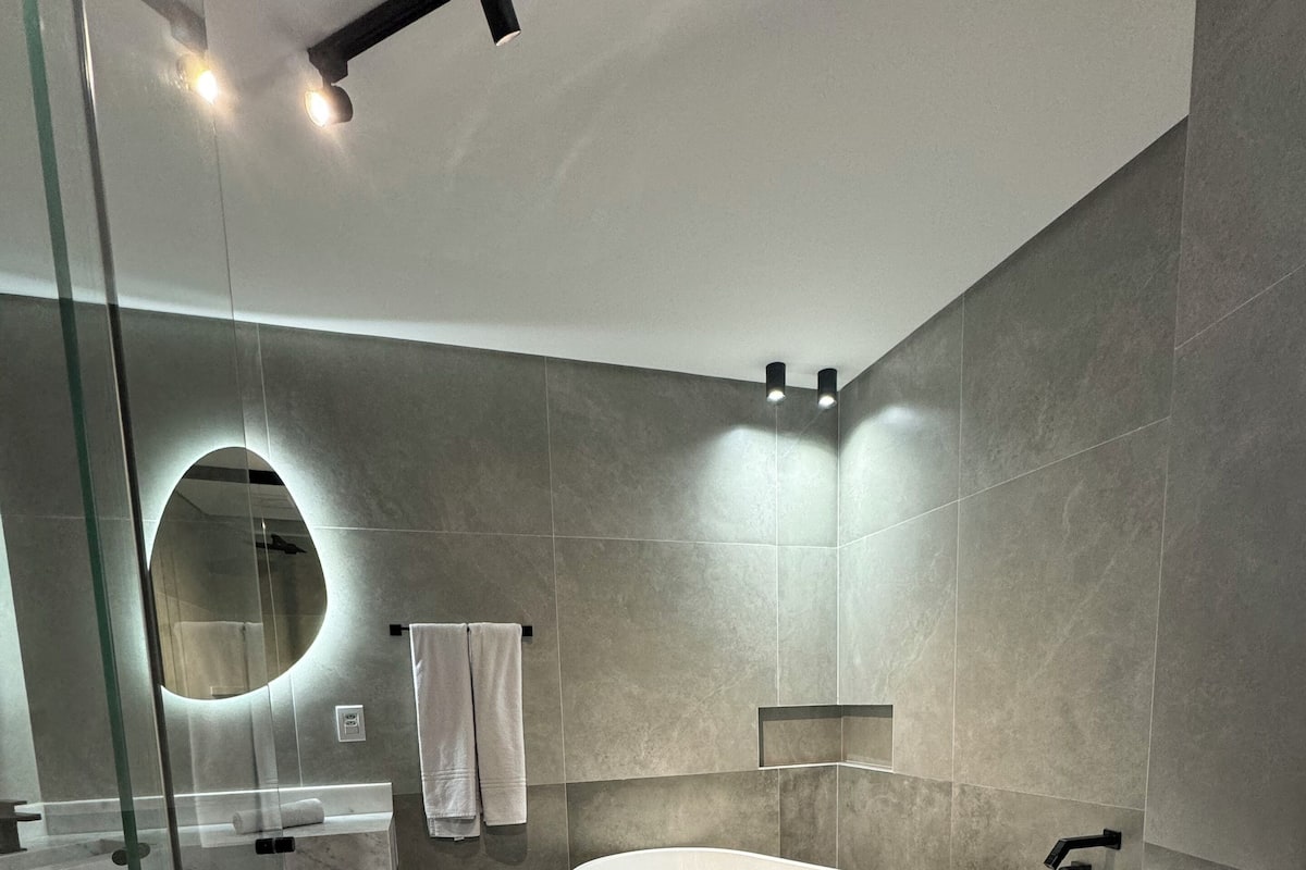 Een moderne badkamer met een vrijstaand bad, een douche met glazen wanden en een wastafelmeubel met spiegel.