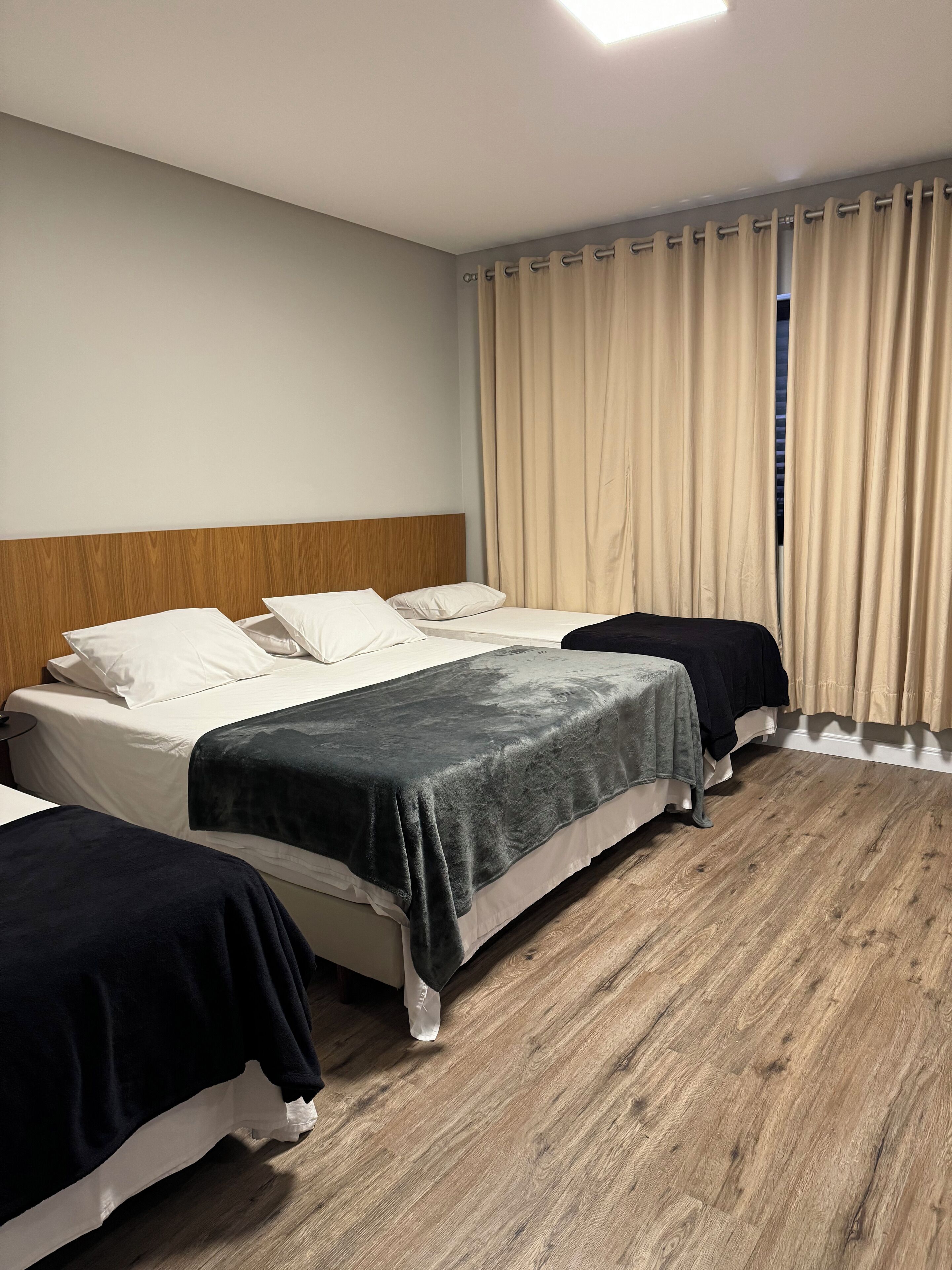 A hotel room with two beds, a wooden headboard, beige curtains, and a wooden floor.