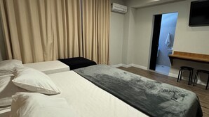 A hotel room with a large bed, a desk, and an air conditioning unit. - Hotel Diamante (São Paulo)