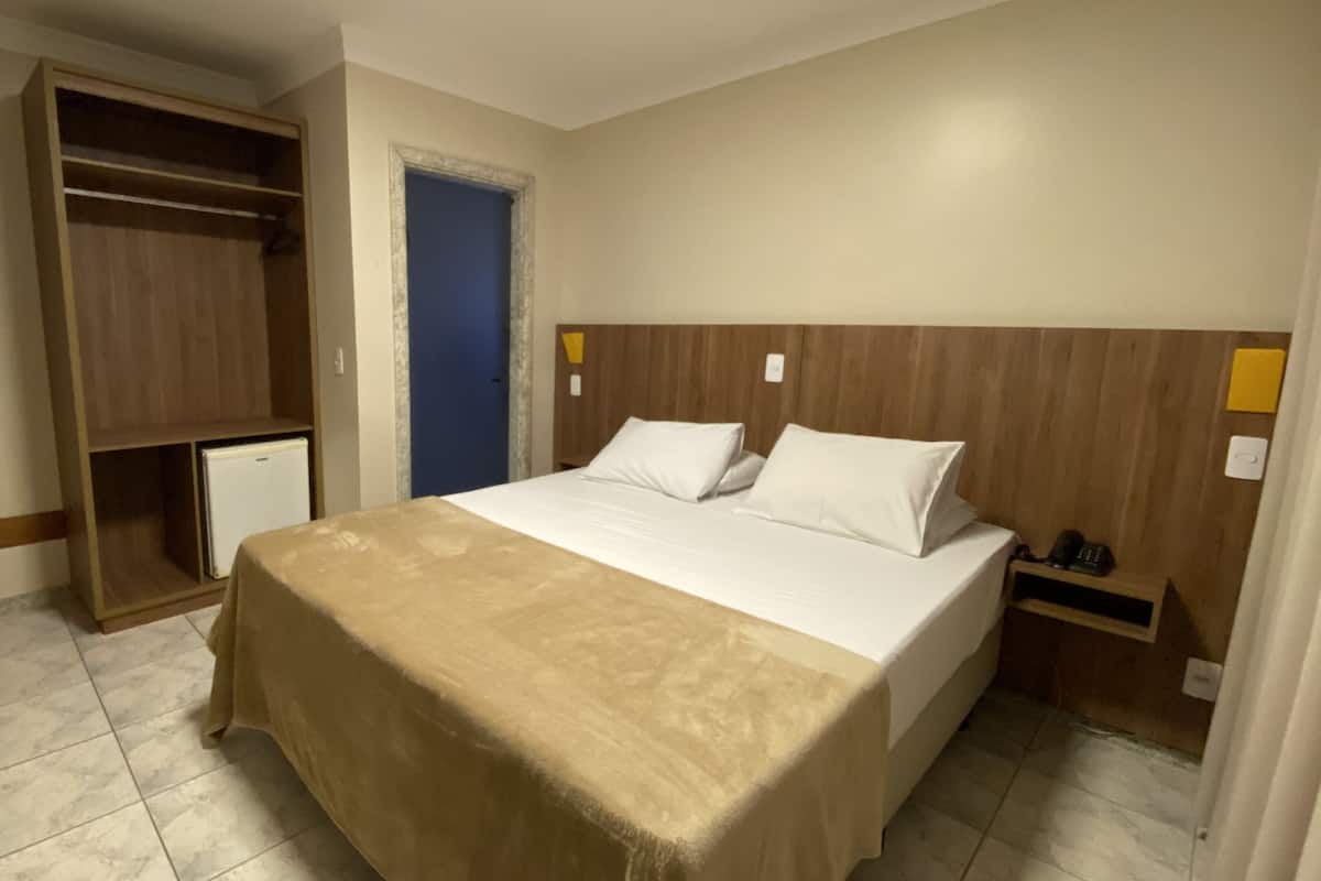 Een hotelkamer met een bed, een kledingkast, een bureau en een klein nachtkastje.