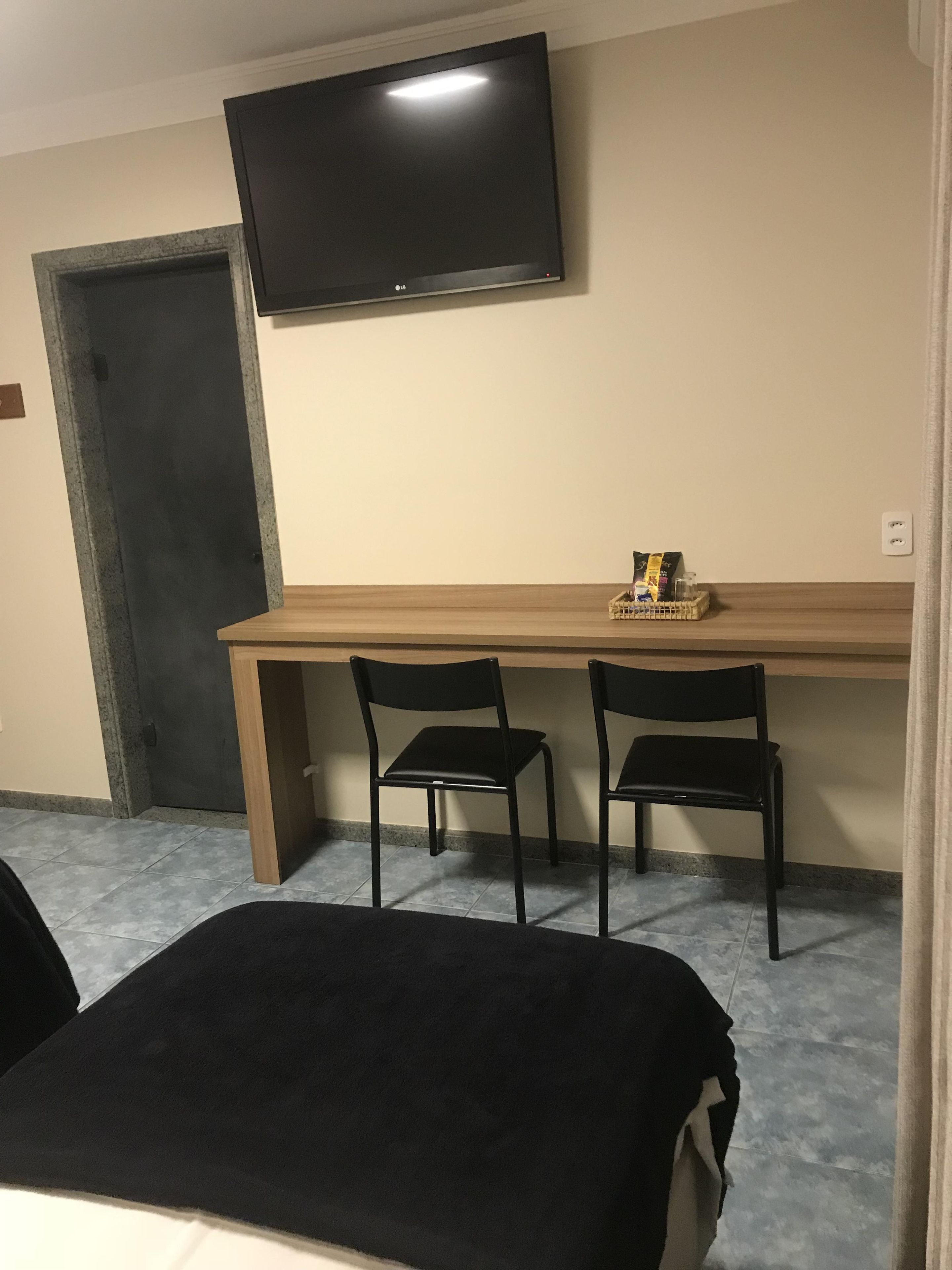 A room with a bed, a desk with two chairs, a television, and a door.