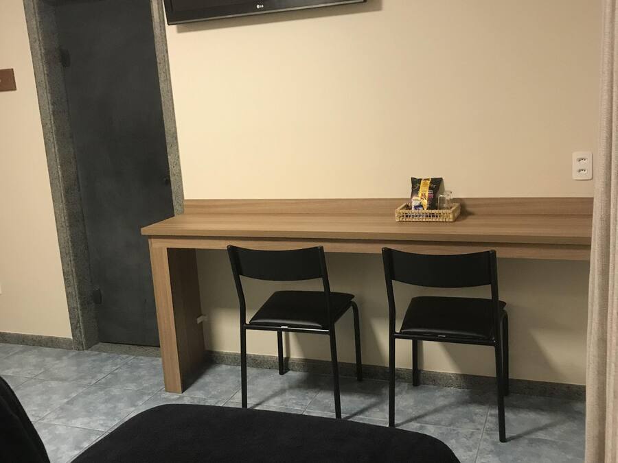 A room with a bed, a desk with two chairs, a television, and a door.