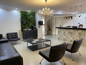 Un área de recepción moderna con un mostrador negro, una lámpara de araña y una pared verde con plantas.