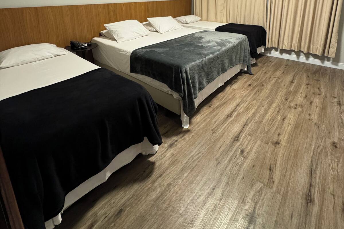 Hotelkamer met twee bedden, houten vloer, een houten hoofdbord, een nachtkastje met telefoon, en beige gordijnen.