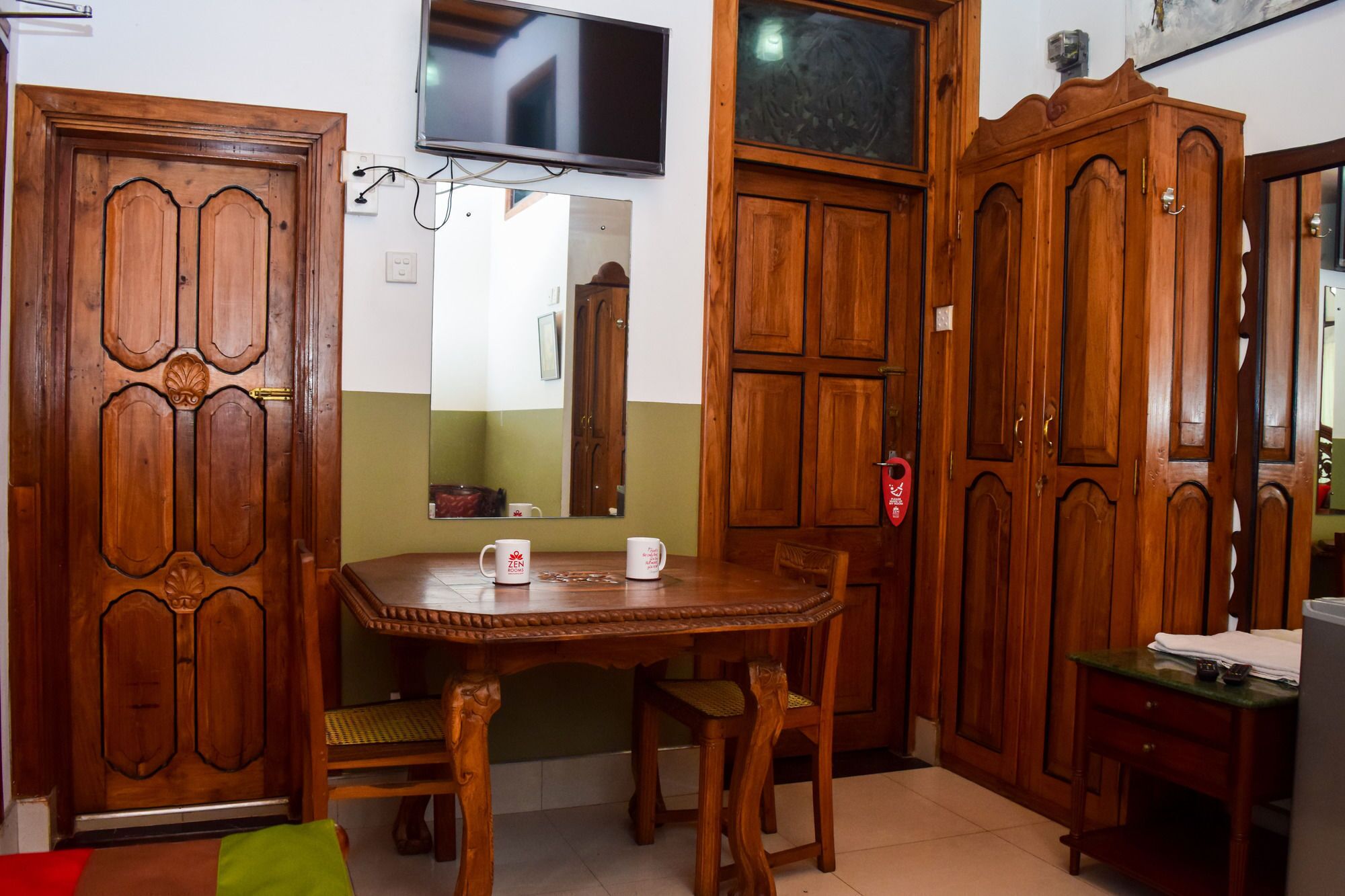 A room with a wooden dining table, chairs, a television mounted on the wall, and wooden cabinets.