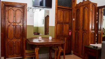 A room with a wooden dining table, chairs, a television mounted on the wall, and wooden cabinets.