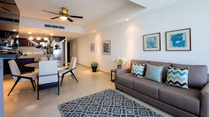 A modern living room with a sofa, a dining area with chairs, a ceiling fan, and artwork on the walls. - Grand Venetian Condominium (Puerto Vallarta)